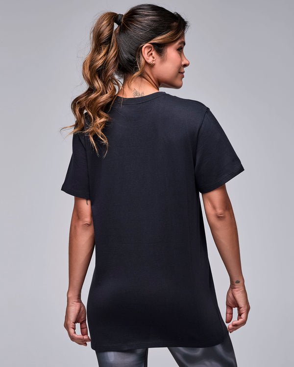 Shown from the back, a female model in the black 'STRONG' tee, with a plain back and relaxed, longer fit.