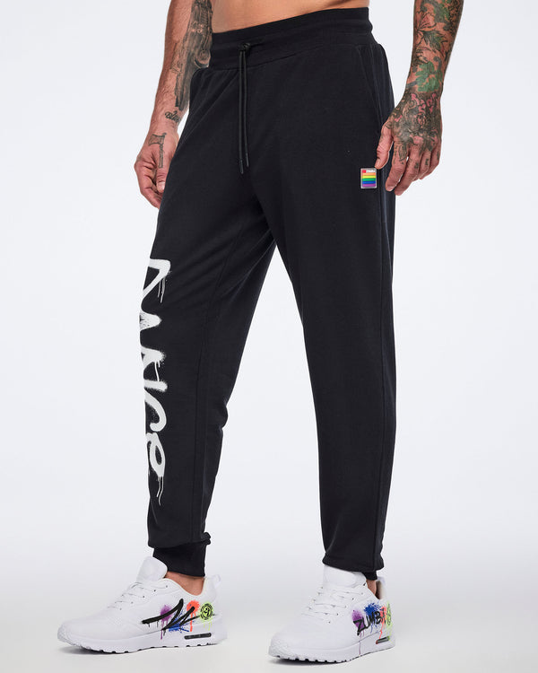 Male model wearing black jogger pants with showing a small rainbow long on the upper left leg and partially visible