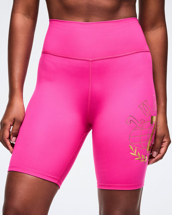 Close-up view of pink biker shorts with a gold logo on a white background.
