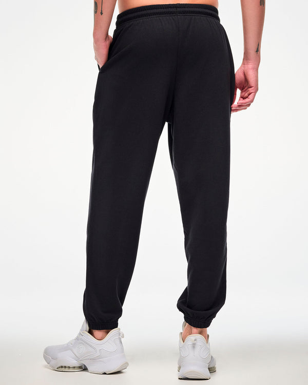 Shown from the back, male model wearing black joggers and white sneakers.