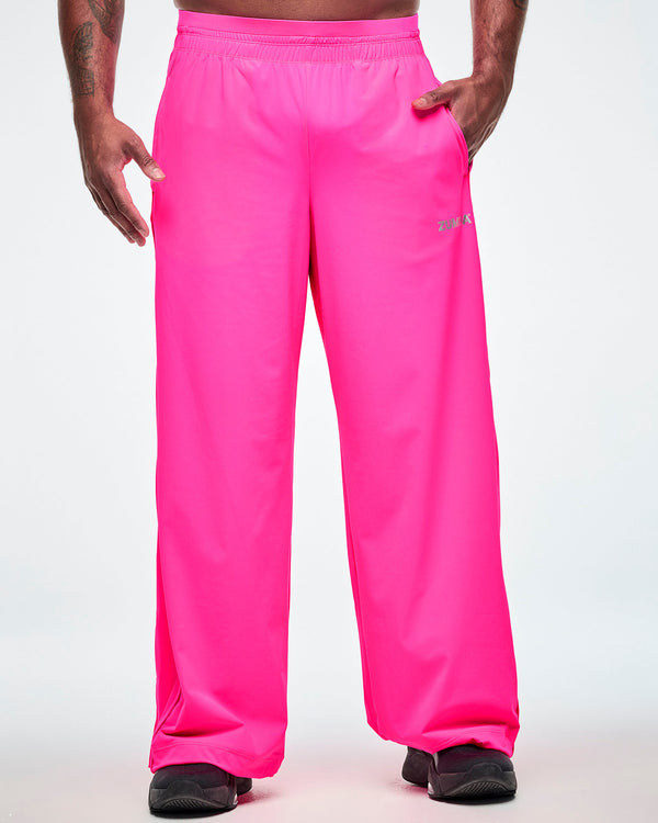 Pink slouch pants worn by a male model, showing the elastic waistband, side pockets, and a small silver ZUMBA text on the upper left thigh.