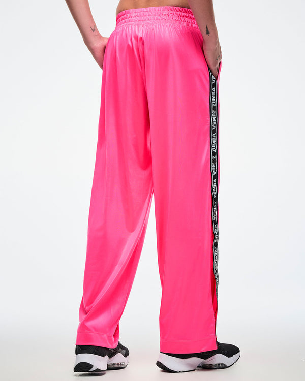 Back view of a male model wearing pink track pants with a black and white Zumba side stripe on a white background.