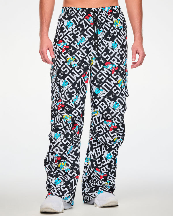 Male model in the black and white Smurfs print oversized cargo pants with a black drawcord waist and cargo pockets on both legs, paired with white shoes.