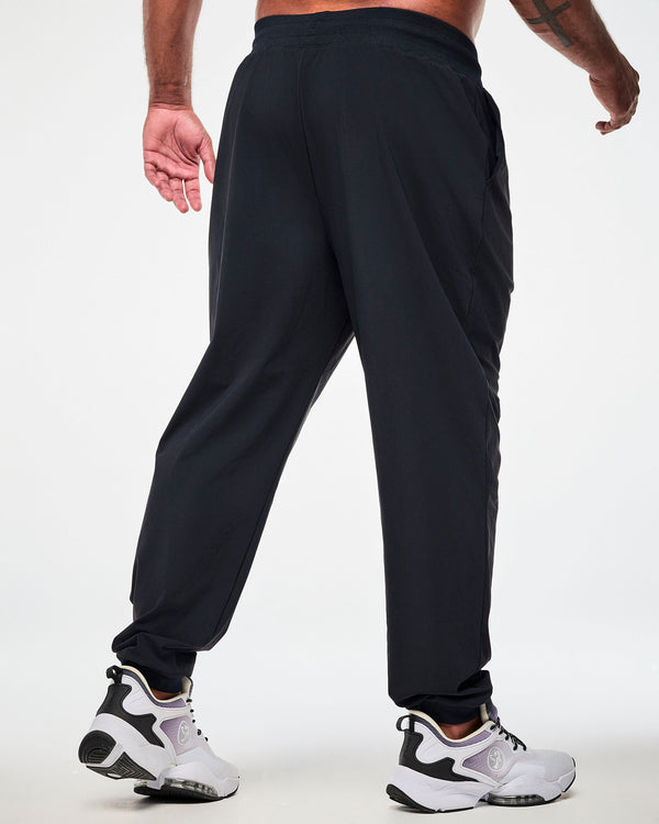 Back view of a male model wearing high waisted black jogger pants, paired with white shoes.
