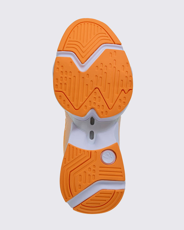 Sole view of the shoe, showing orange grooved tread split into forefoot and heel sections on a white sole, with a white Zumbito logo disc at the heel.