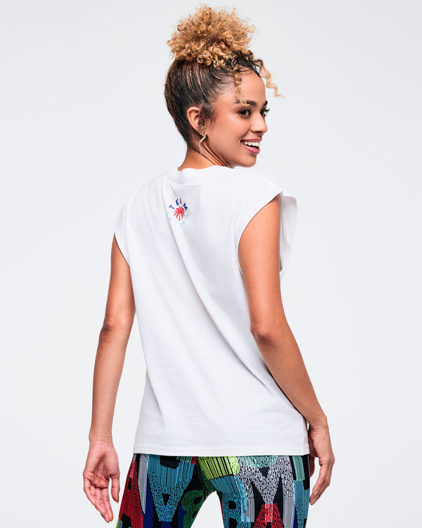 Back view of the white sleeveless muscle tee on a female model, showing the relaxed fit and small logo detail near the back neckline, paired with multicolor patterned leggings.