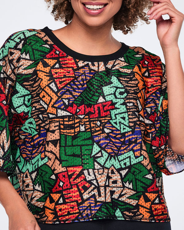 Close-up of the multicolor abstract-print cropped mesh top, highlighting the black crew neckline, mesh fabric, and loose short sleeves over black leggings.