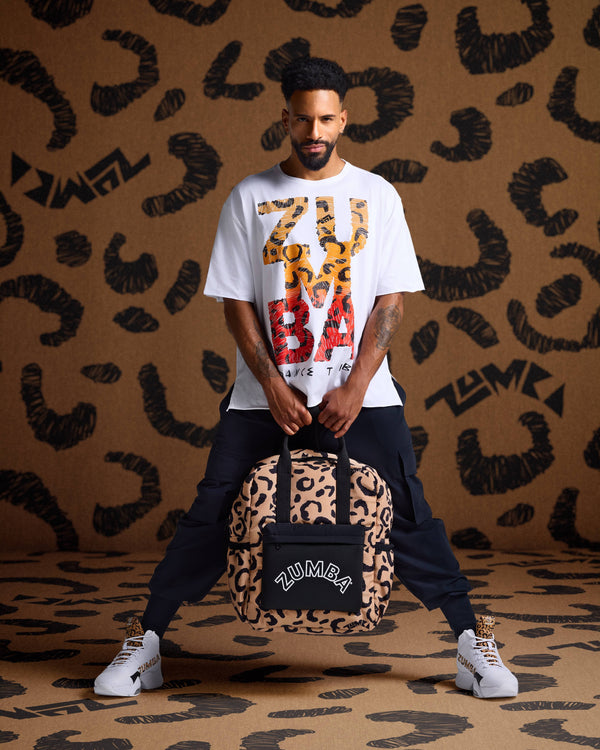 Leopard print backpack held by a male model in a white graphic tee, black cargo joggers, and white high-top sneakers against leopard print backdrop.