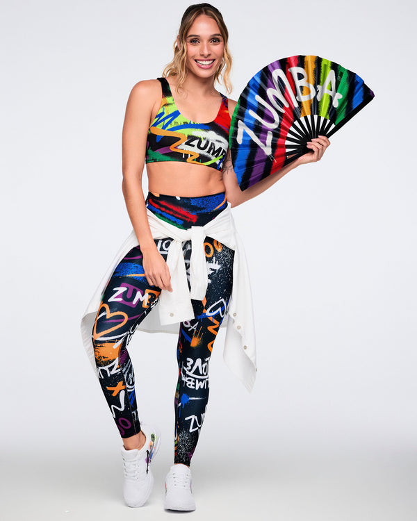 Female model wearing colorful Zumba outfit with a fan on a white background.