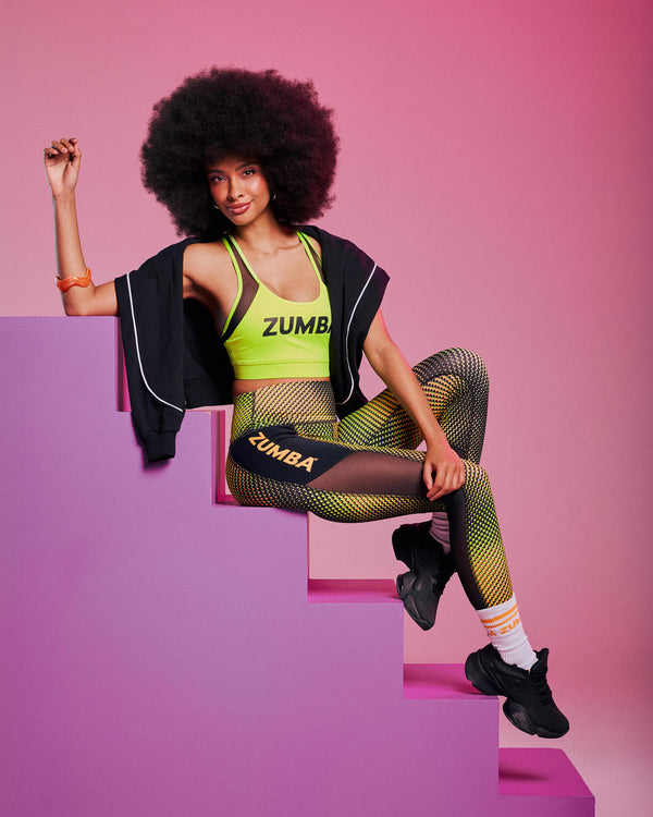 Female model with an afro seated on pink steps, wearing a yellow-green