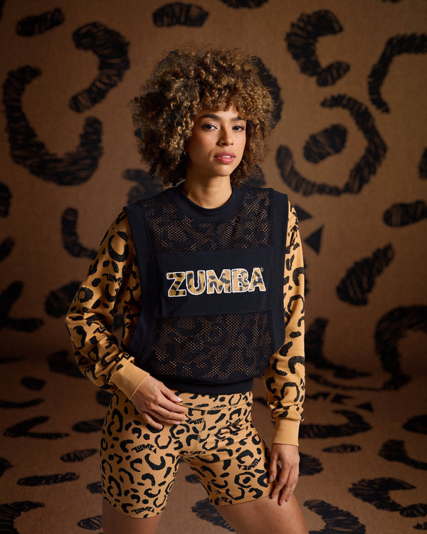 Black mesh Zumba top on female model with a leopard print sweatshirt underneath with biker shorts against a tan leopard backdrop.