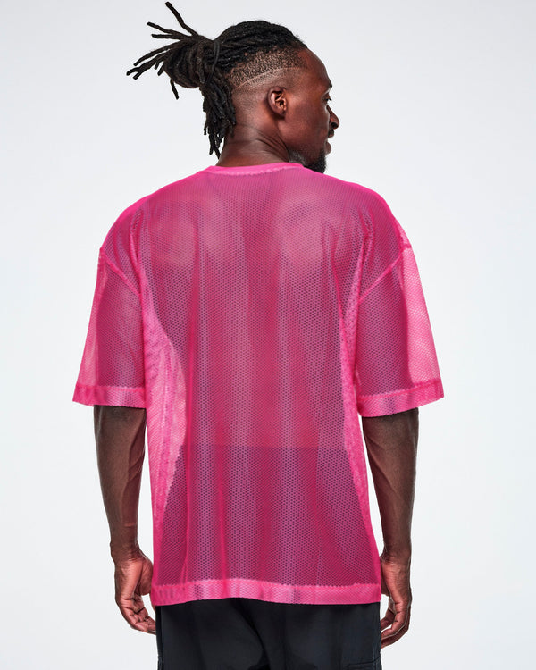 Back view of a male model wearing a pink mesh Zumba top, paired with black pants.