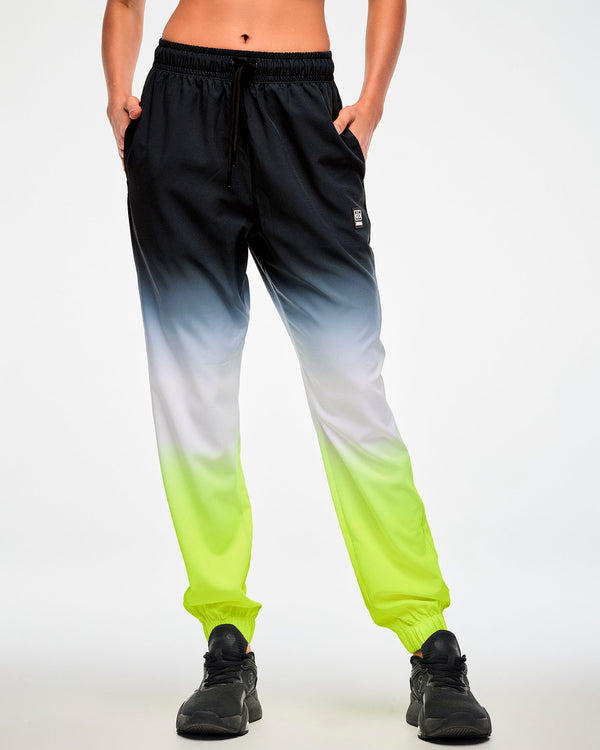 Female model wearing black-to-neon-yellow ombre joggers with a drawstring waist, paired with black sneakers, hands in both side pockets.