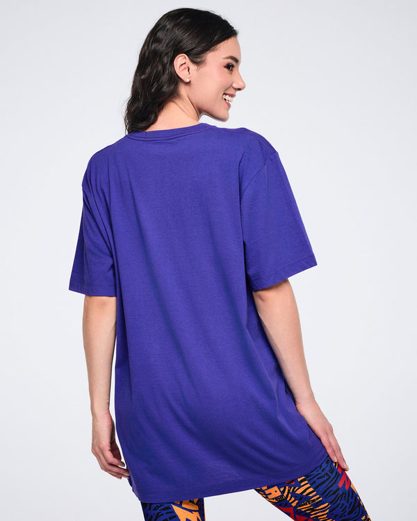 Female model shown from the back wearing an oversized purple short-sleeve T-shirt with a relaxed fit, paired with blue, orange, and black patterned leggings.