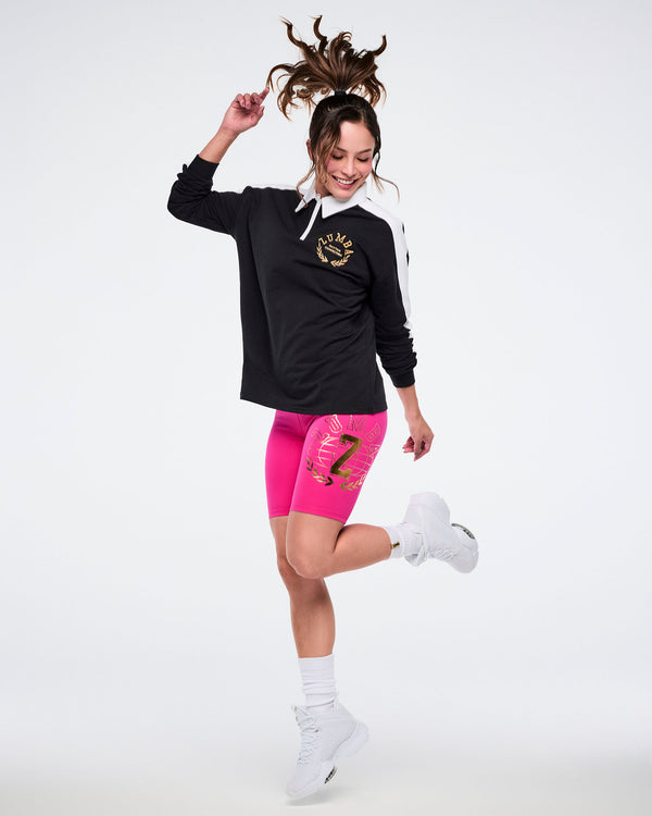 Female model in black polo, pink shorts, white socks and shoes posing on a white background.