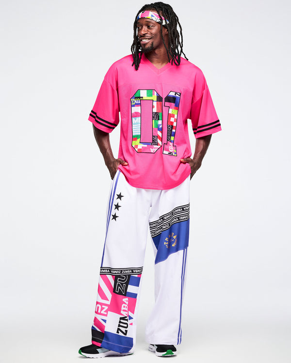 Male model wearing a pink mesh sports top with colorful designs and white pants with patterns, standing against a white background.