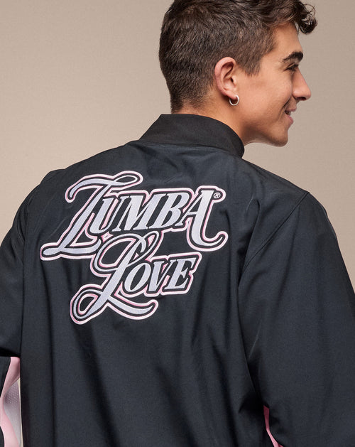 Man wearing a black unisex jacket, that says Zumba Love on the back, in an indoor studio setting.