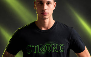 Male model wearing a black crew neck tee with neon green outlined 'STRONG' text over a green wave-like graphic, framed from the chest up. Dark background with diagonal neon light beams.
