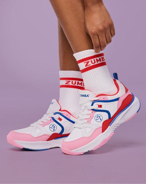 Zumba dance sneakers in white, pink, red, and blue with white crew socks, shown on model adjusting sock hem.