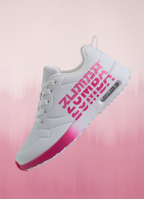 White Zumba sneakers with pink gradient sole and bold pink “Zumba” side logos shown floating on a soft pink backdrop.