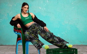 Banner showing a wide lifestyle shot of a female model reclining on stacked colorful chairs with her feet on a green crate, set against a teal wall.