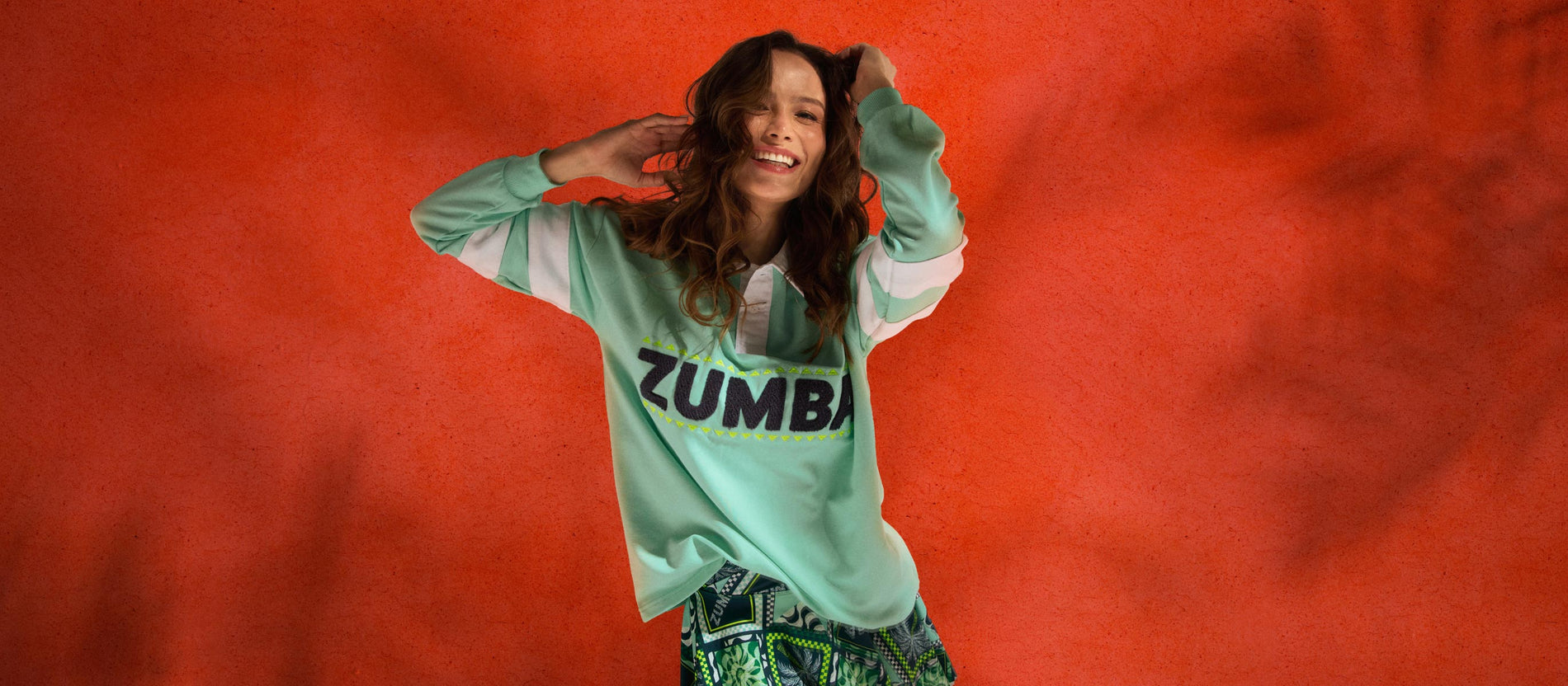 Female model posing playfully in front of a large textured orange backdrop.