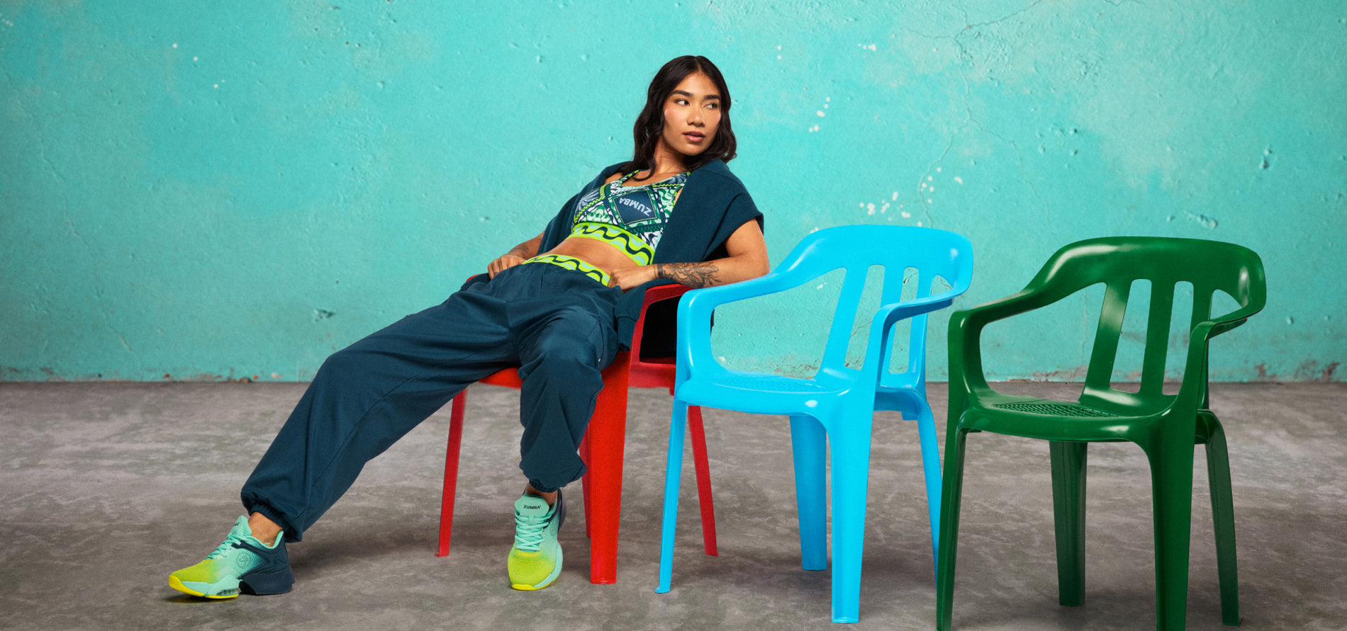 Main Banner showing a wide lifestyle shot of a female model lounging across colorful plastic chairs in front of a distressed teal wall.