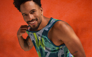 Close-up action portrait of a male model in a ZUMBA tank, smiling against a textured orange backdrop.