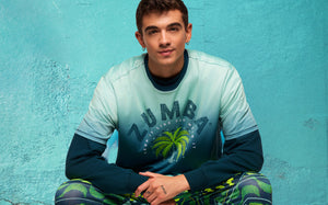 Close-up lifestyle portrait of a male model wearing a ombre t-shirt, seated against a textured teal wall.