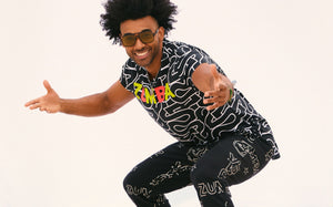A male model wears a black short-sleeve Zumba graphic shirt and matching black printed joggers against a white backdrop.