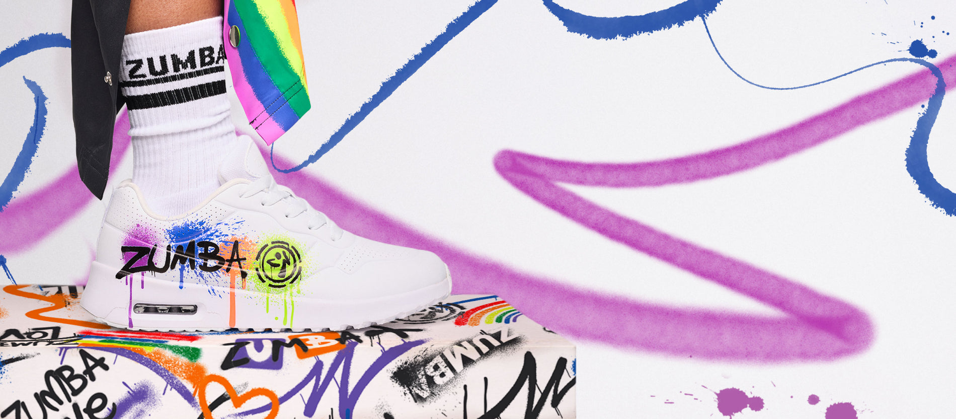 White Zumba sneaker with rainbow paint splashes on a graffiti box and colorful swirl background.