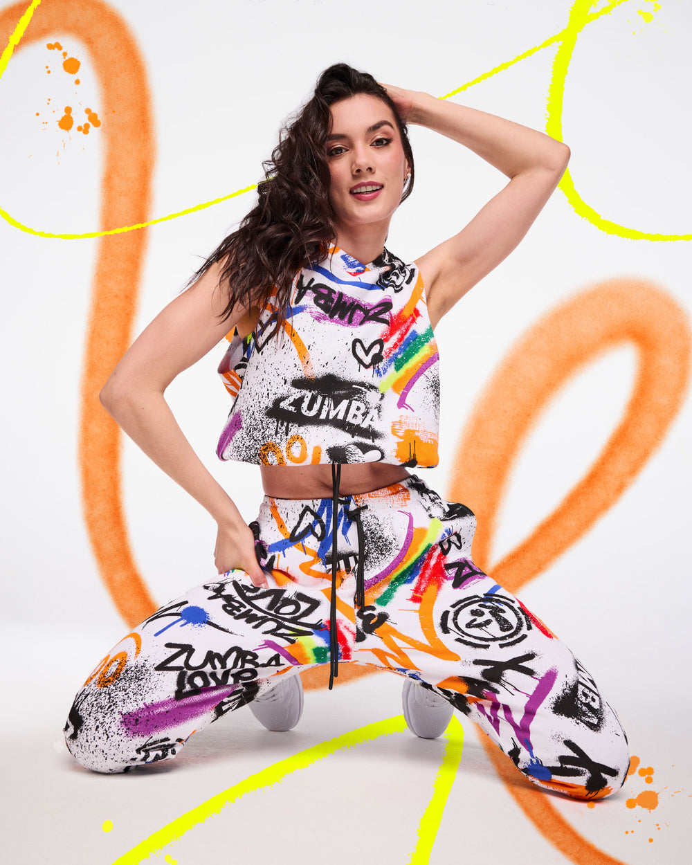 Colorful graffiti‑print workout set on a kneeling female model against a white background with bright spray‑paint accents.