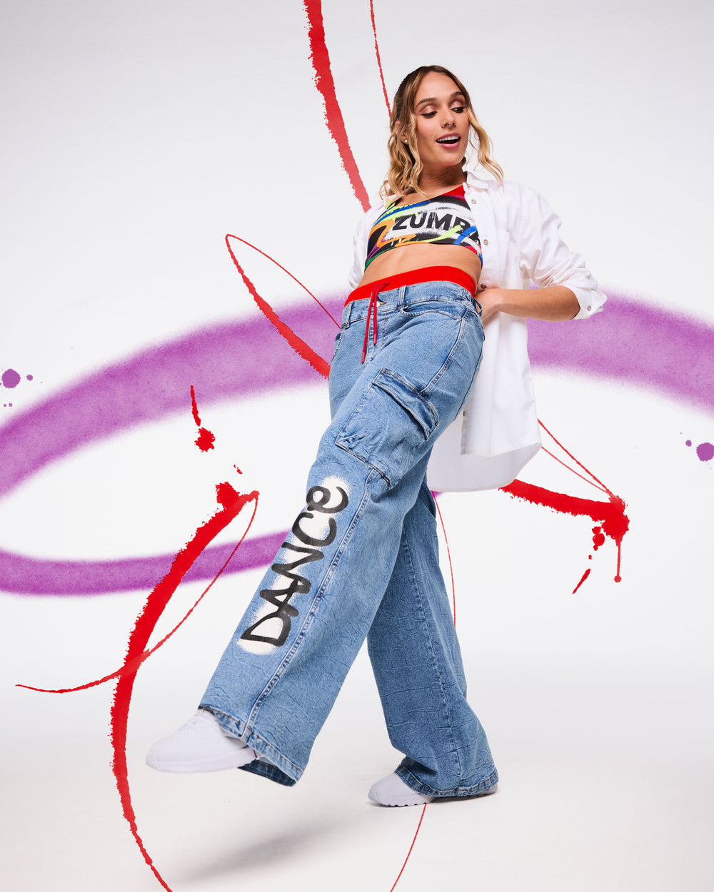 Female model in wide‑leg jeans with “DANCE” graphic, rainbow crop top, white shirt, and bold paint‑stroke background.