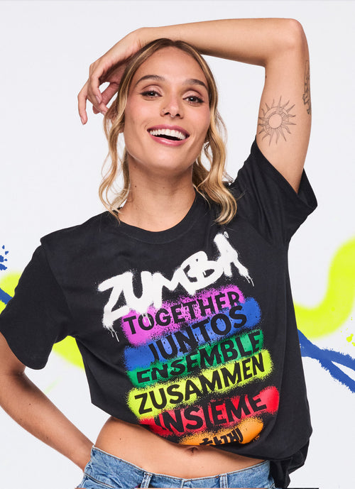 Female model in a black graffiti‑print tee posing with one hand lifted to her head and the other placed behind her back amid a white background with neon paint strokes.