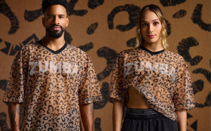 Male and female models wearing matching cheetah print mesh Zumba tops with the female black shorts visible,  against a cheetah background.