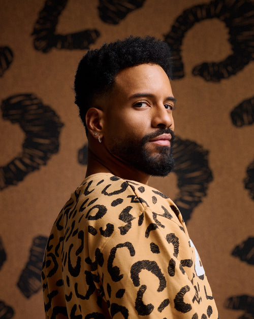 Male model wearing a tan Zumba top with cheetah print against a matching cheetah background.