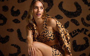 Closer view of a female model in a cheetah print bra and shorts with a matching sweatshirt draped over her shoulders, against a cheetah print backdrop.
