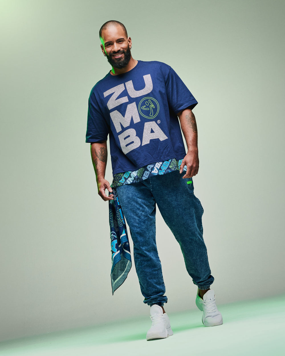Banner of a male model wearing a blue “Zumba” T-shirt with blue denim pants and a bandana hanging from his pocket, set against a light green background.
