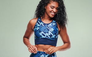Female model wearing matching Zumba patterned bra and leggings on a mint background.