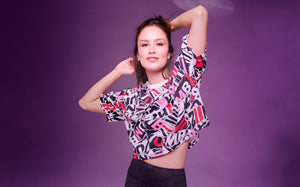 A female model poses in a colorful ZUMBA graphic crop top against a purple gradient background.
