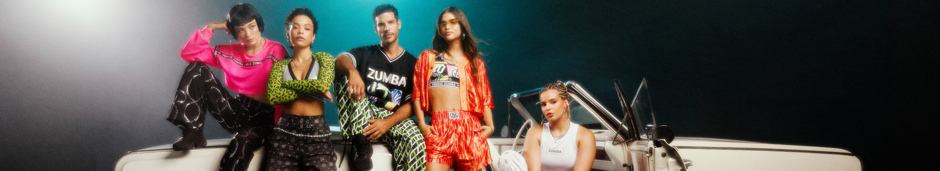 A group of five models posing together in vibrant, patterned streetwear clothing, including green and black patterned tops and bottoms, a bright pink top, and an orange patterned button down and boxer shorts, set against white vintage convertible and a dark black and blue background.