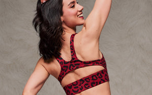 Back view of a female model shown wearing a dark red leopard print racerback bra with a keyhole cutout above the wide underband. Taupe faux fur backdrop.