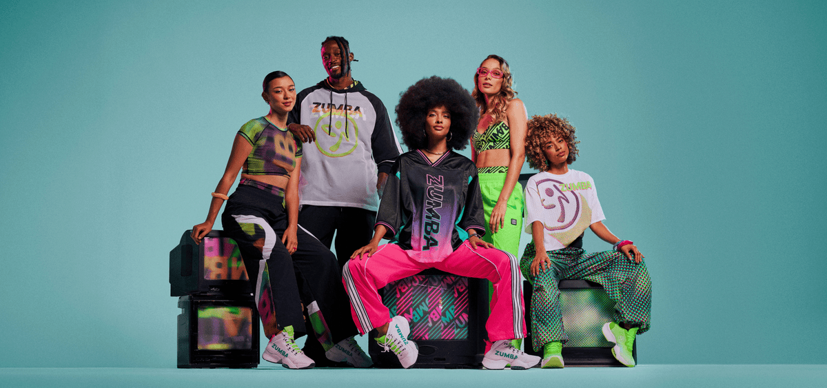 Group of male and female models wearing various Zumba Wear — crop top with track pants, a mesh Zumbito hoodie, gradient 
