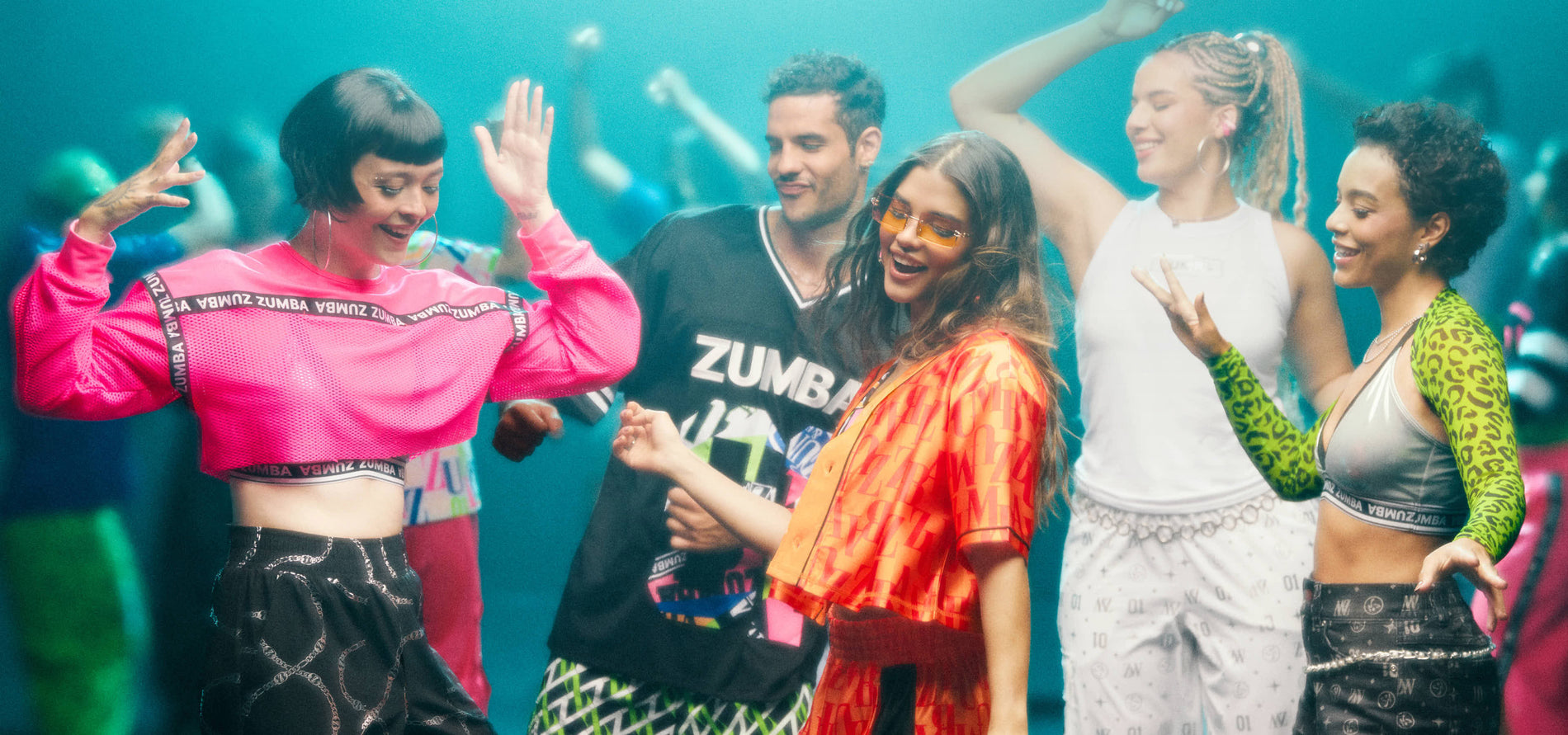 Banner showing a diverse group of Zumba dancers in vibrant activewear—pink mesh crop top, black Zumba jersey, orange monogram shirt, white tank, and silver bra with green leopard top —smiling and moving together in a lively studio scene.