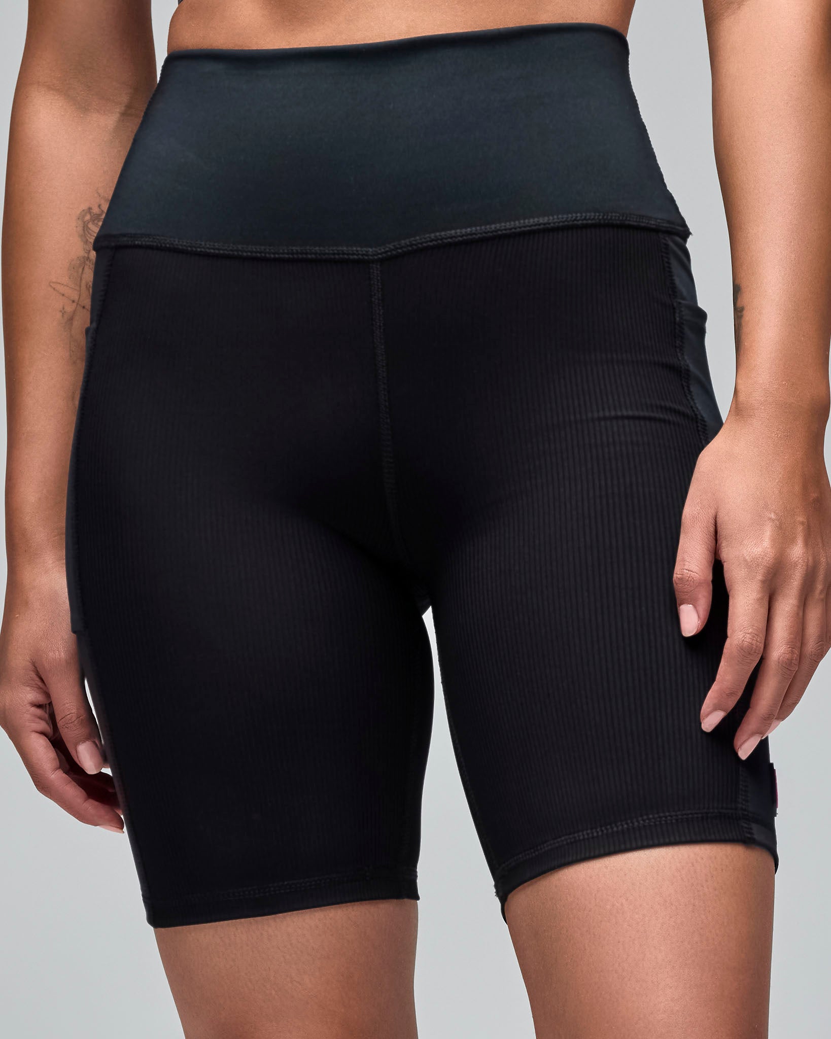 Black high-waisted biker shorts with a smooth waistband and ribbed texture through the legs. Female model wears the fitted mid-thigh shorts in a front view against a light gray background.