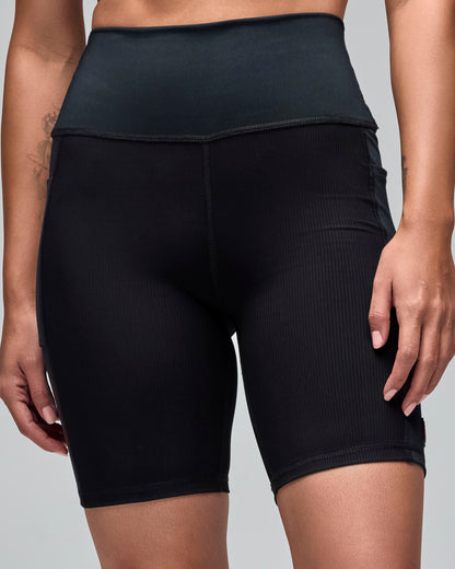 Black high-waisted biker shorts with a smooth waistband and ribbed texture through the legs. Female model wears the fitted mid-thigh shorts in a front view against a light gray background.