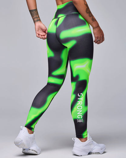 Back view of a female model in the neon green and black swirl print leggings, with white 'STRONG iD' text running down the back of the right calf.