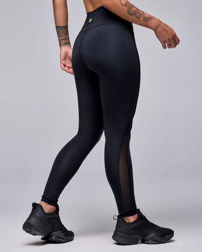 Shown from the back, the black mesh insert leggings, with a small neon green logo tag at the back waistband and mesh visible along the outer calf.