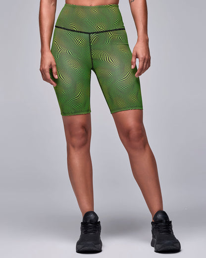 Neon green and black wavy check print biker shorts on a female model, with a high waistband and mid-thigh length, paired with black shoes.