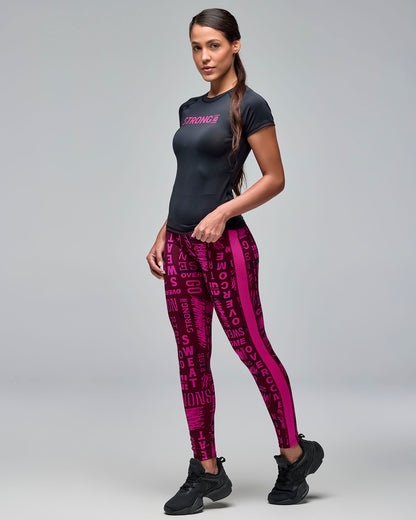 Black fitted short-sleeve performance top with bright pink “STRONG iD” text on the chest. Female model wears the crewneck athletic tee with burgundy and pink printed leggings and black sneakers against a light gray background.